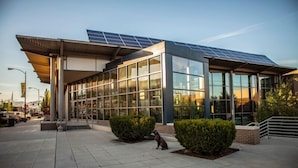Un bâtiment moderne doté de grandes fenêtres en verre et d’un toit recouvert de panneaux solaires.