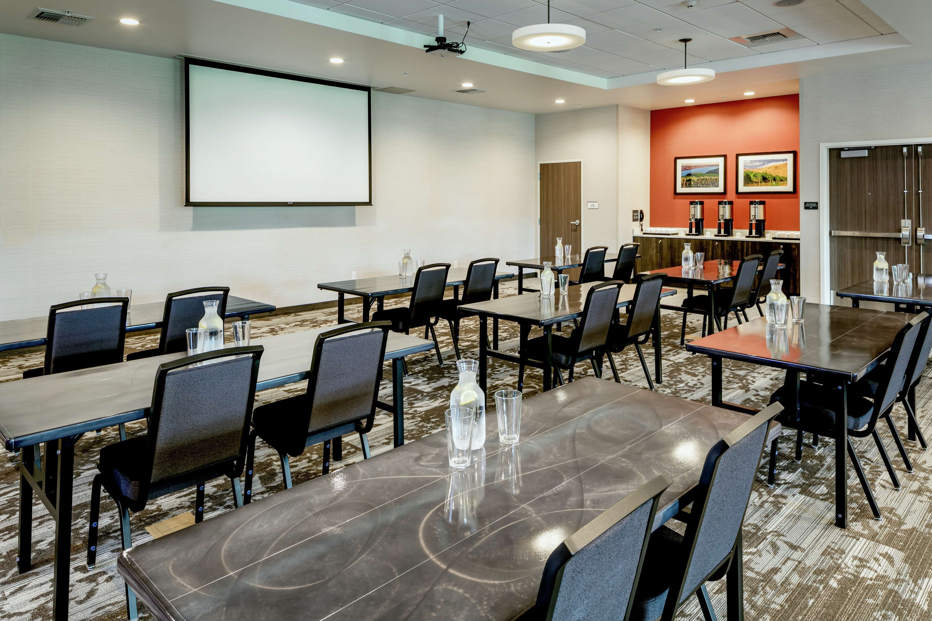 A conference room with a large screen, multiple tables, and chairs.
