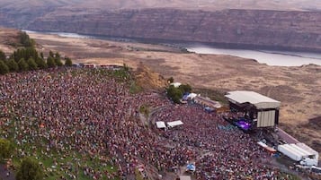 An outdoor concert with a large crowd and a stage set up on a hill overlooking a valley.