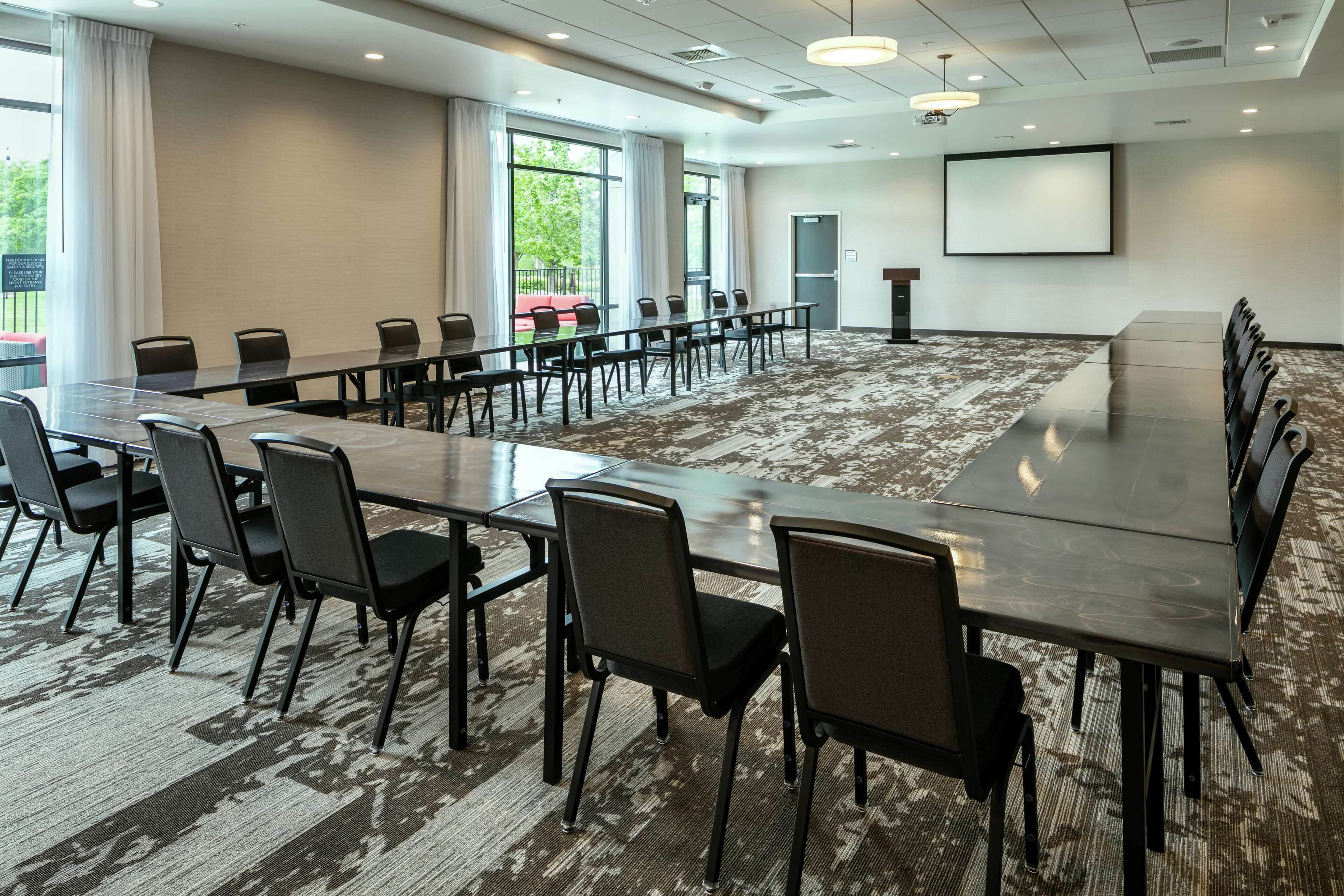 Une salle de conférence dotée d’une longue table et de chaises, de grandes fenêtres, d’un écran de projection et d’un sol recouvert de moquette.