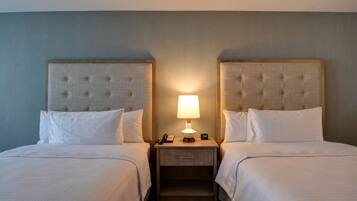 A hotel room with two beds, a nightstand with a lamp, and a phone.
