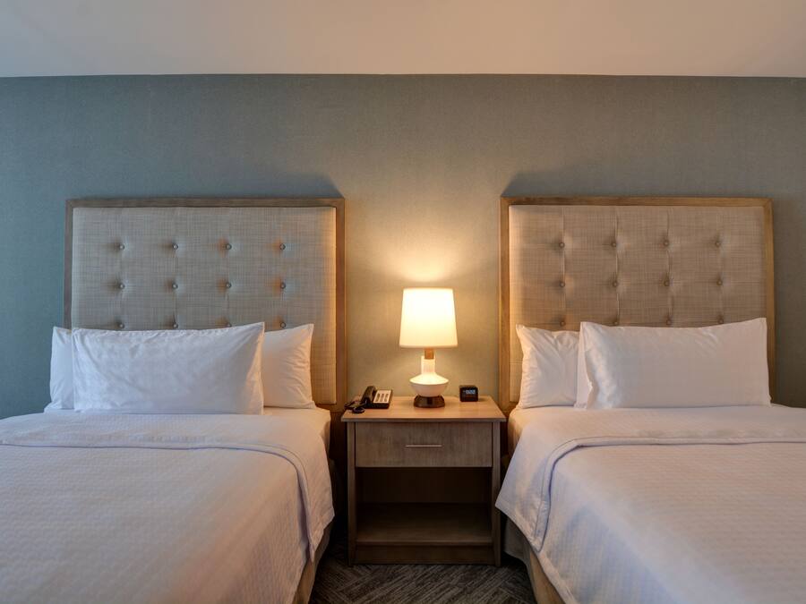 A hotel room with two beds, a nightstand with a lamp, and a phone.