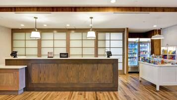 A hotel reception area with a wooden reception desk, two pendant lights, a minibar, and a refrigerator stocked with beverages.