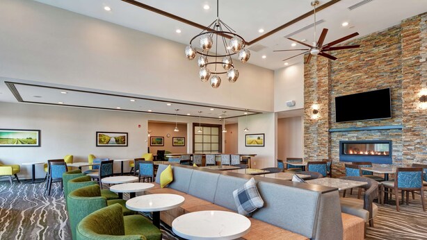 A modern hotel lobby with a seating area, a fireplace, and a television mounted on a stone wall. - Homewood Suites by Hilton Hadley Amherst (Hadley)