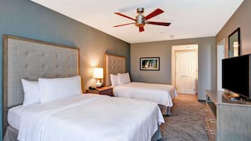 A hotel room with two beds, a ceiling fan, a TV, and a door leading to another room.