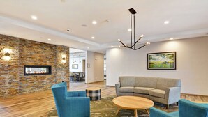 A modern lounge area with a stone wall, a fireplace, a sofa, and two blue armchairs. - Homewood Suites by Hilton Hadley Amherst (Hadley)