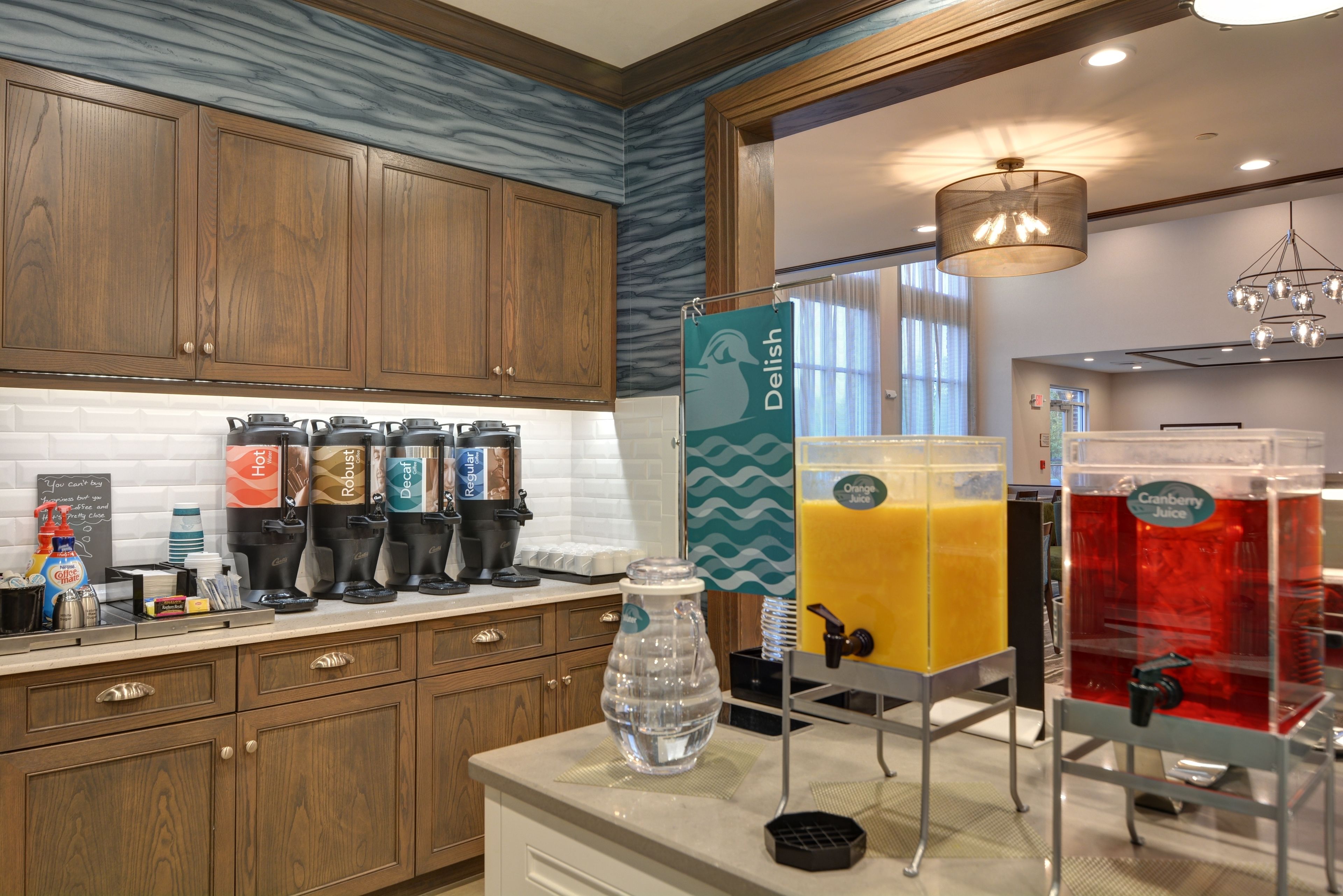 A kitchen with wooden cabinets, a water dispenser, and juice dispensers labeled with different flavors.