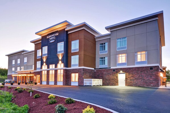 A modern hotel with a brick facade, multiple windows, and a well-lit entrance. - Homewood Suites by Hilton Hadley Amherst (Hadley)