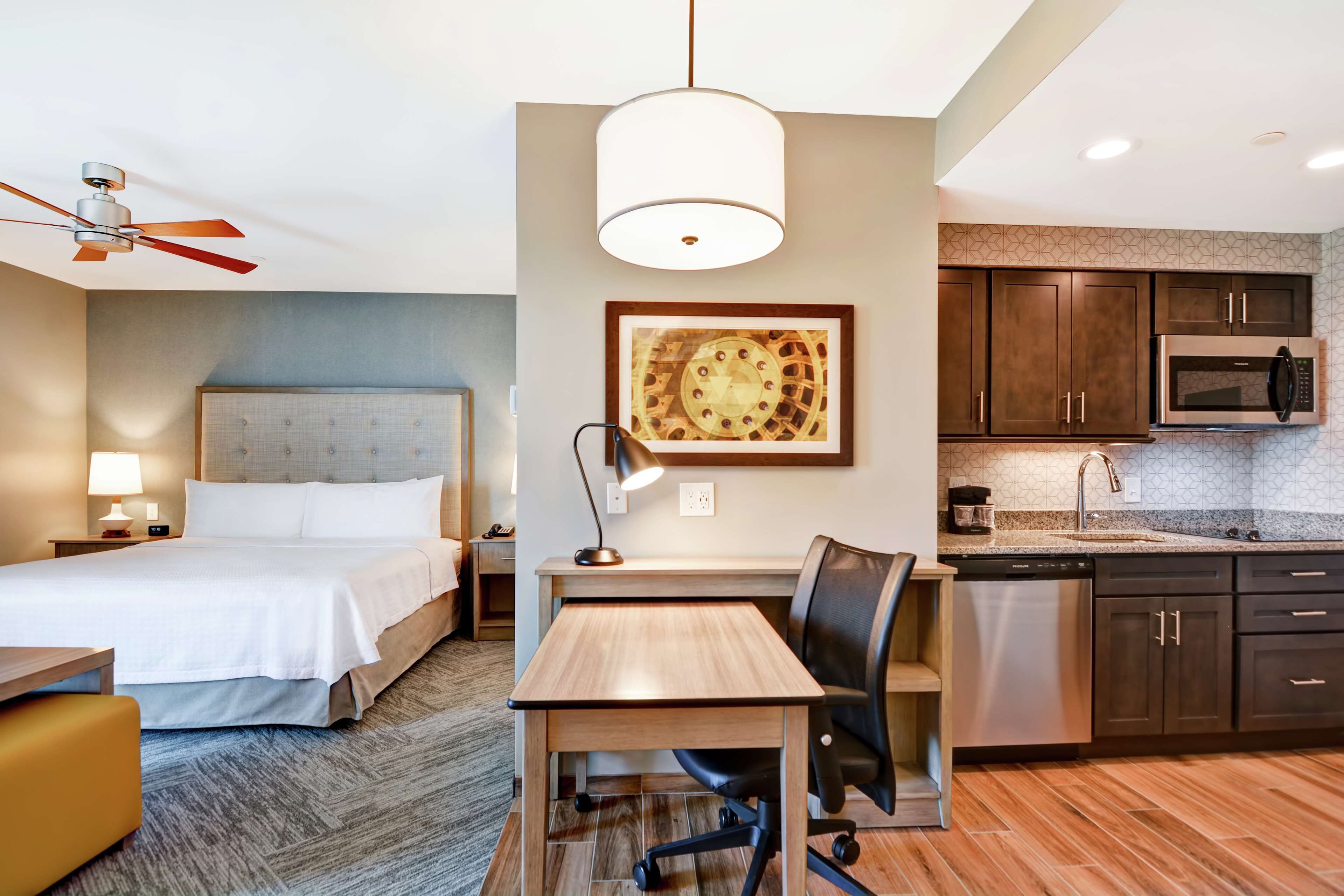A hotel room with a bed, desk, chair, and kitchenette.