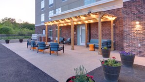 An outdoor seating area with chairs and tables, a covered patio with string lights, and potted plants. - Homewood Suites by Hilton Hadley Amherst (Hadley)