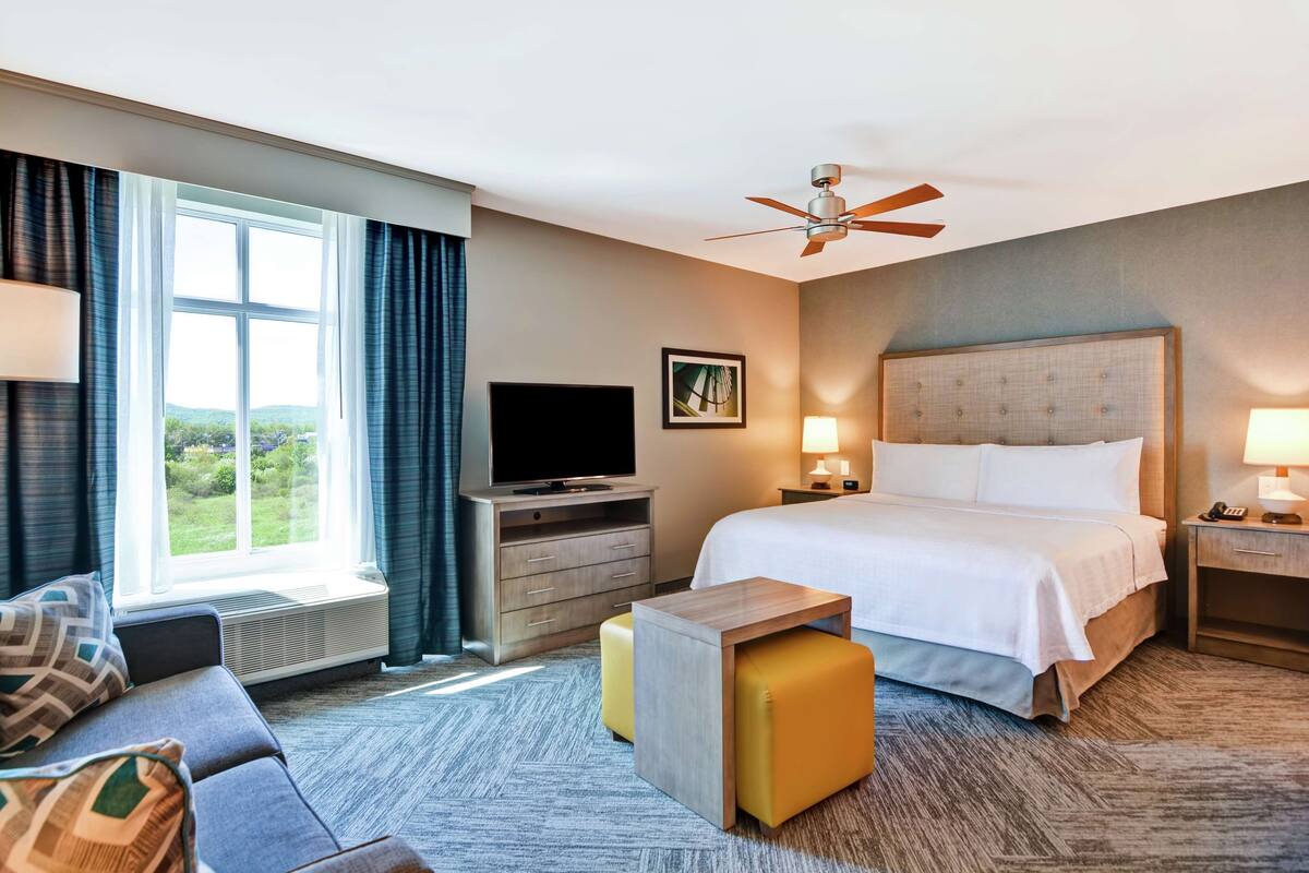 A hotel room with a bed, a television, a desk, a chair, and a window with curtains.