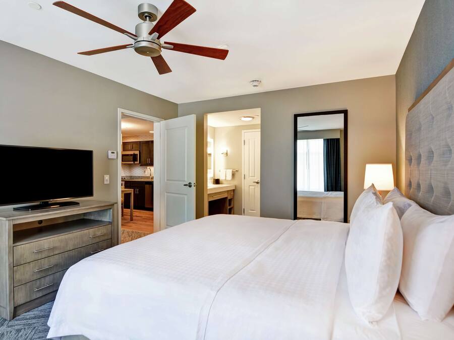 A hotel room with a bed, a television on a wooden dresser, a ceiling fan, and a bathroom visible through an open door.
