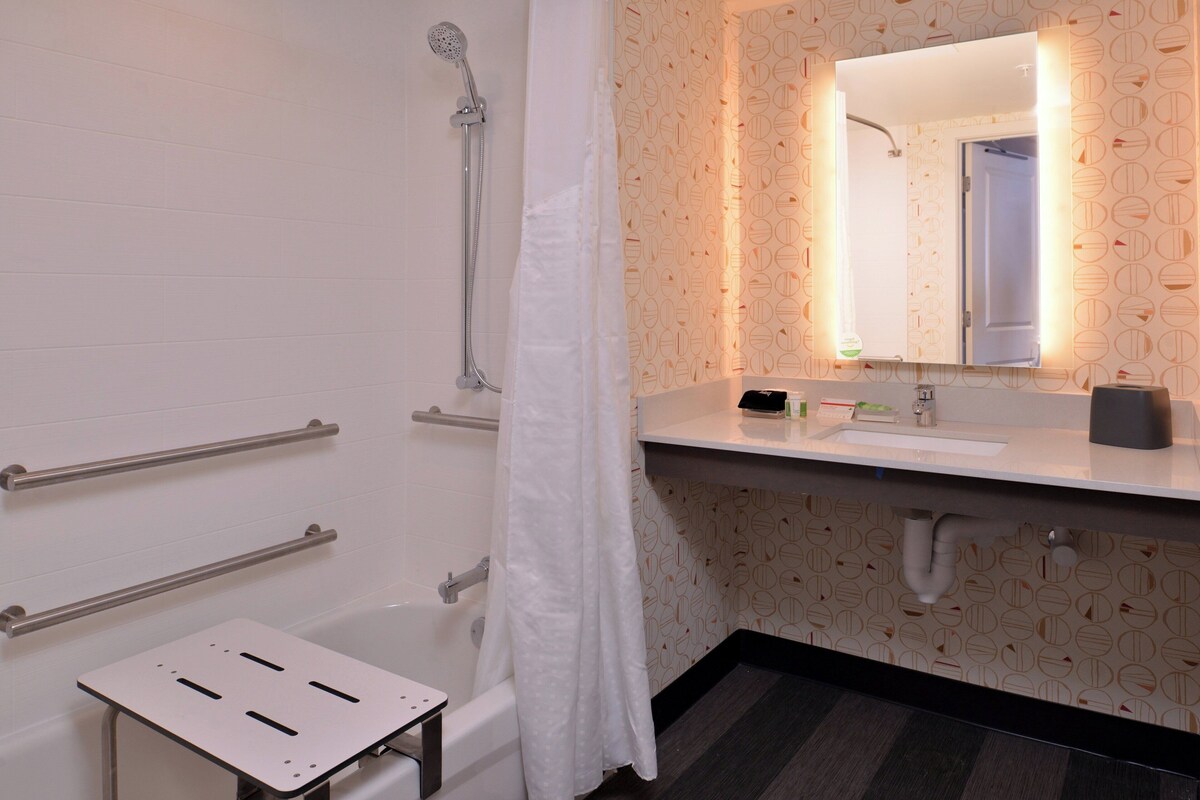 Een badkamer met een bad, een douche, een wastafel met spiegel en een handdoekrek.