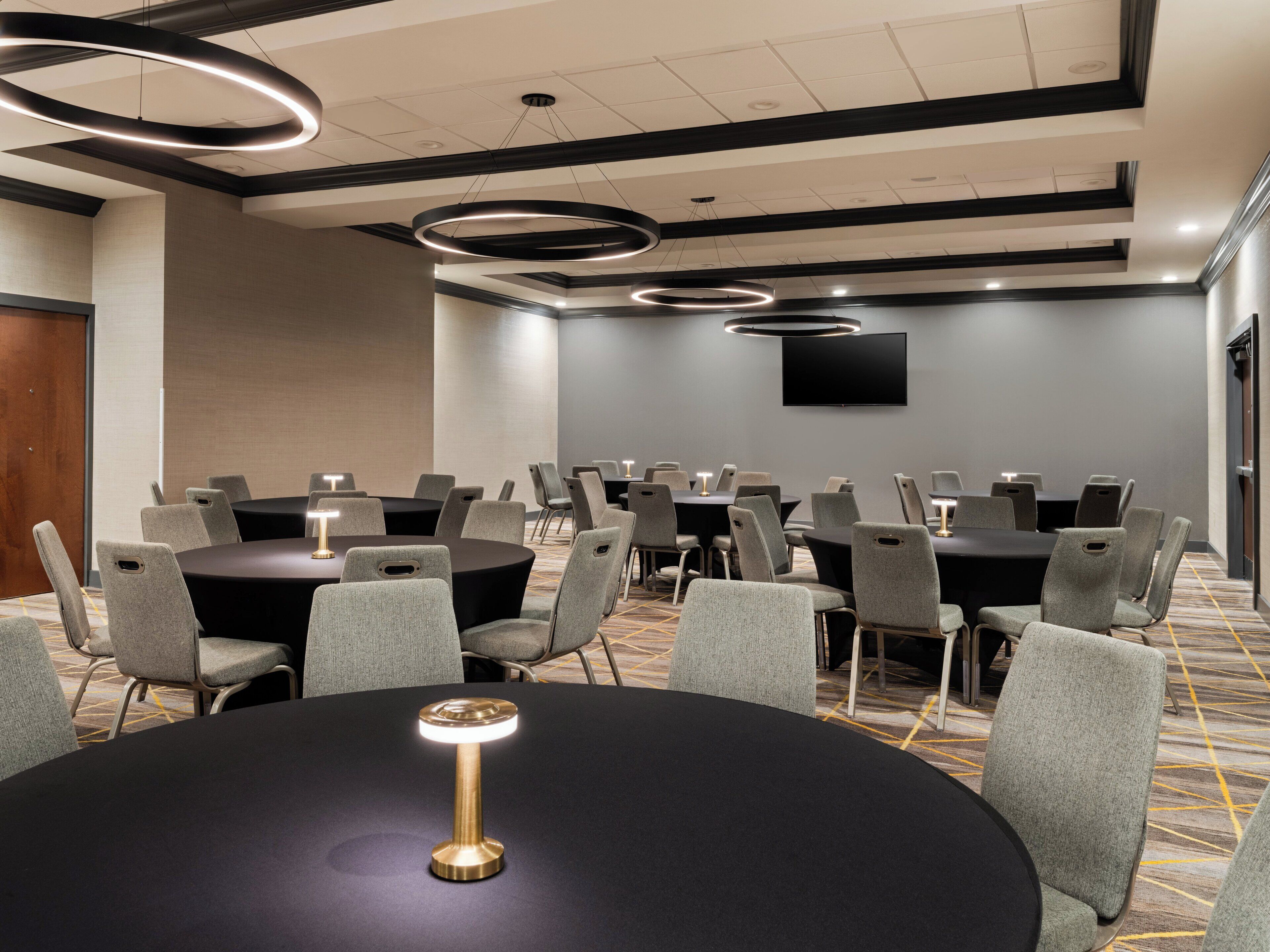 A conference room with round tables and grey chairs, a flat-screen TV on the wall, and a modern ceiling design.