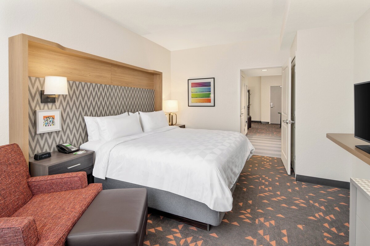 Hotelkamer met een bed, bureau, stoel, televisie, lamp en een foto aan de muur.
