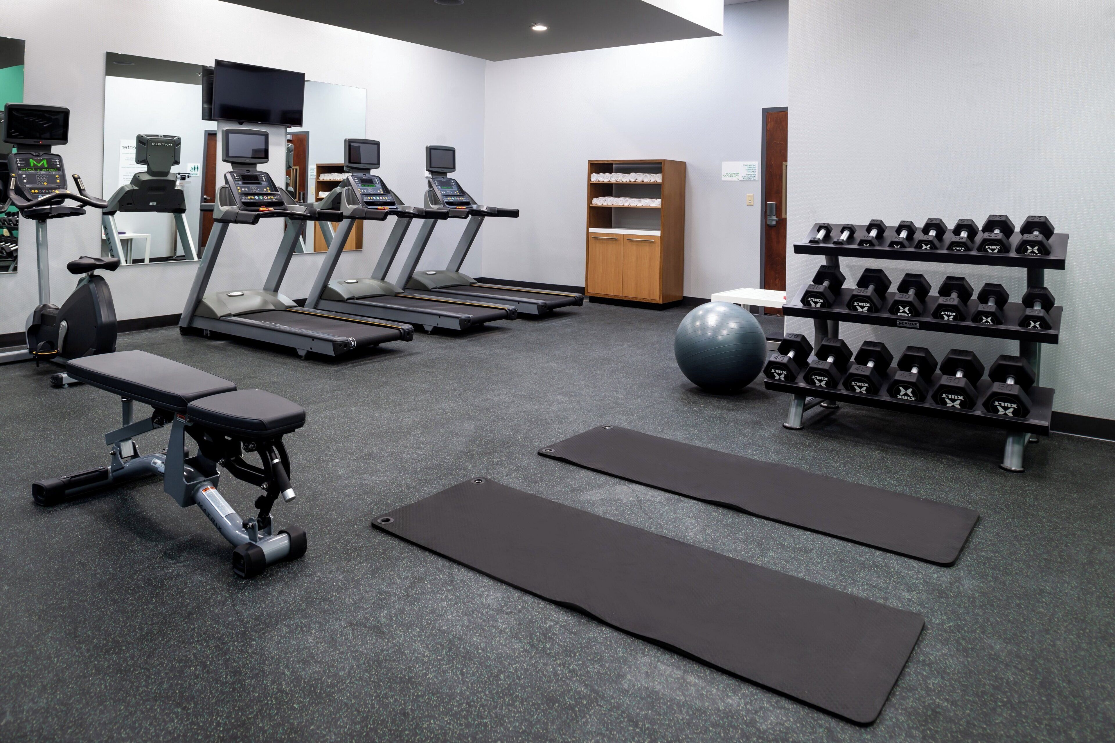 A gym with treadmills, a stationary bike, dumbbells, and exercise mats.