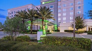 A Holiday Inn & Suites building with a modern design, featuring a covered entrance and a well-maintained landscaped area with palm trees and shrubs.