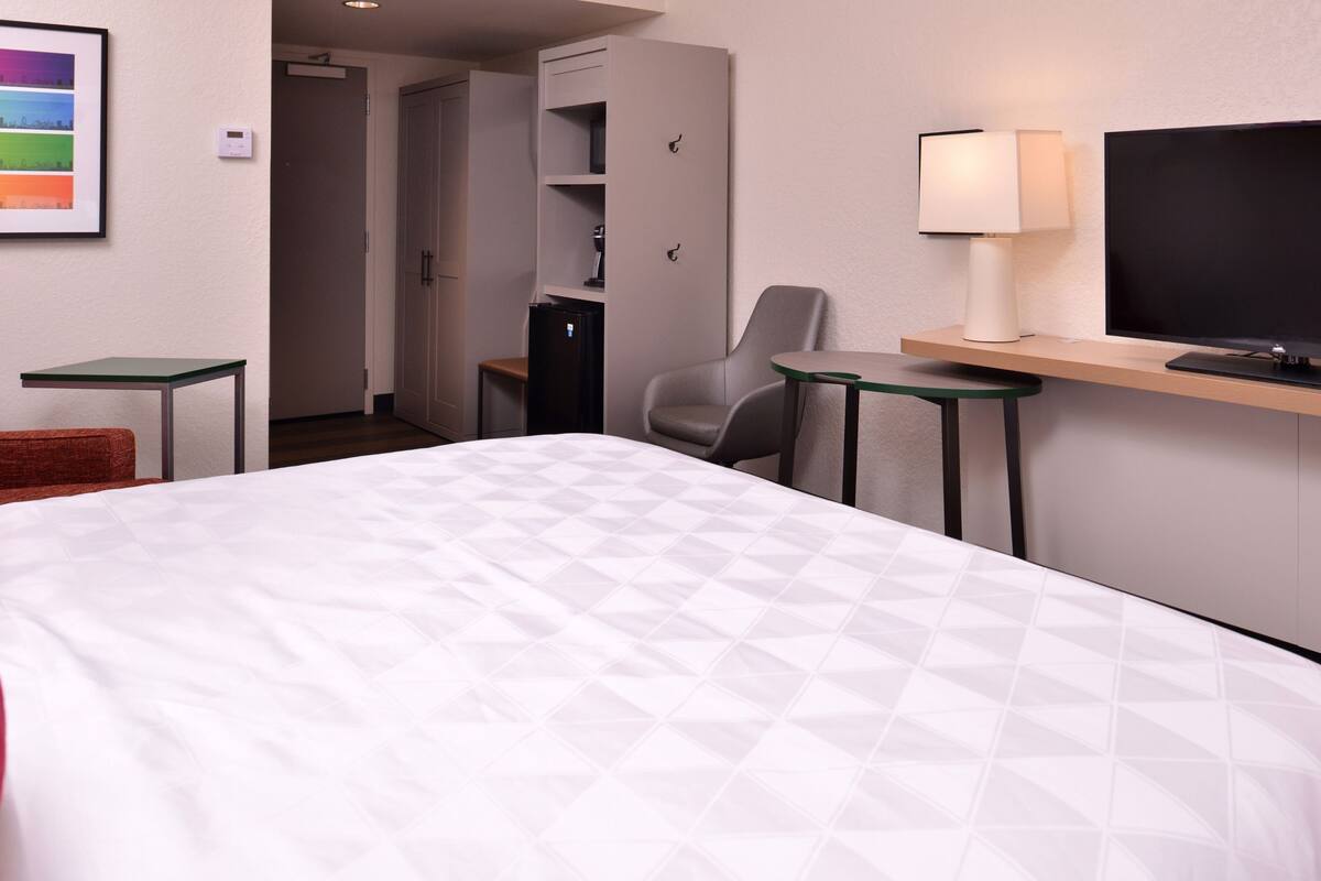 Een hotelkamer met een bed, een bureau met een computer, een stoel, een televisie en een kledingkast.