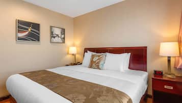 A hotel room with a large bed, two bedside tables, a nightstand, a clock, and two wall-mounted artworks.
