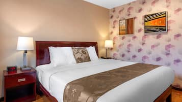 Une chambre d’hôtel avec un grand lit, deux tables de chevet, une commode et un mur recouvert d’un papier peint à motifs géométriques, ainsi que deux tableaux.