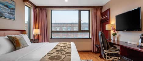 Habitación de hotel con una cama grande, un escritorio con ordenador, un televisor de pantalla plana y una ventana con cortinas.