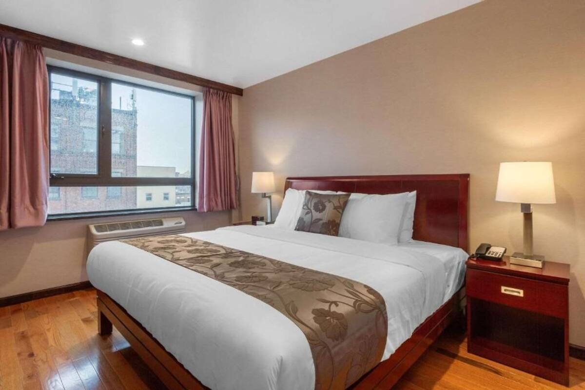 A hotel room with a large bed, two bedside lamps, a nightstand with a phone, and a window with curtains.