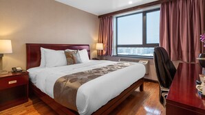 Una habitación de hotel con una cama grande, dos mesitas de noche con lámparas, un escritorio con silla y un ventanal con cortinas.