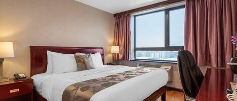 Quarto de hotel com uma cama grande, duas mesas de cabeceira com abajures, uma escrivaninha com cadeira e uma janela com cortinas.