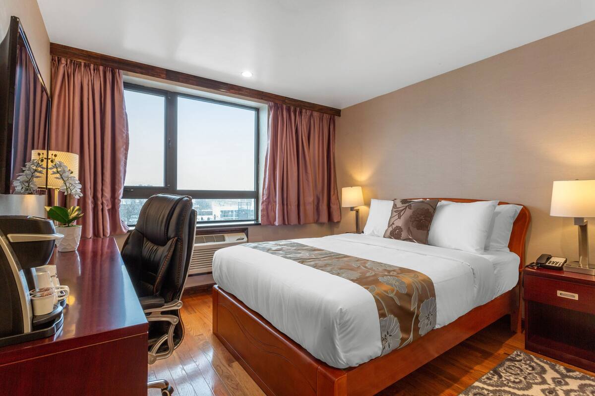 A hotel room with a large bed, a desk with a telephone, a chair, a desk lamp, and a window with curtains.