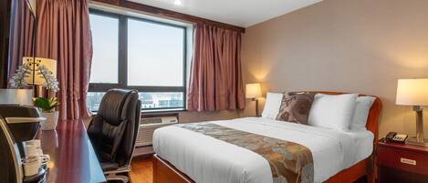 Hotelkamer met een groot bed, een bureau met telefoon, een stoel, een bureaulamp en een raam met gordijnen.