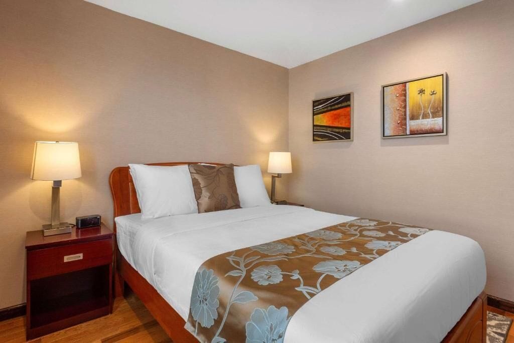 A hotel room with a bed, two bedside tables, lamps, and two wall-mounted artworks.