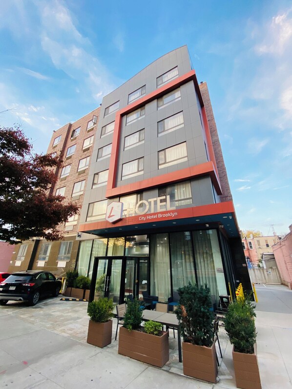 A modern hotel building with a prominent "HOTEL" sign, large windows, and outdoor seating area with planters. - The L Hotel (Brooklyn)