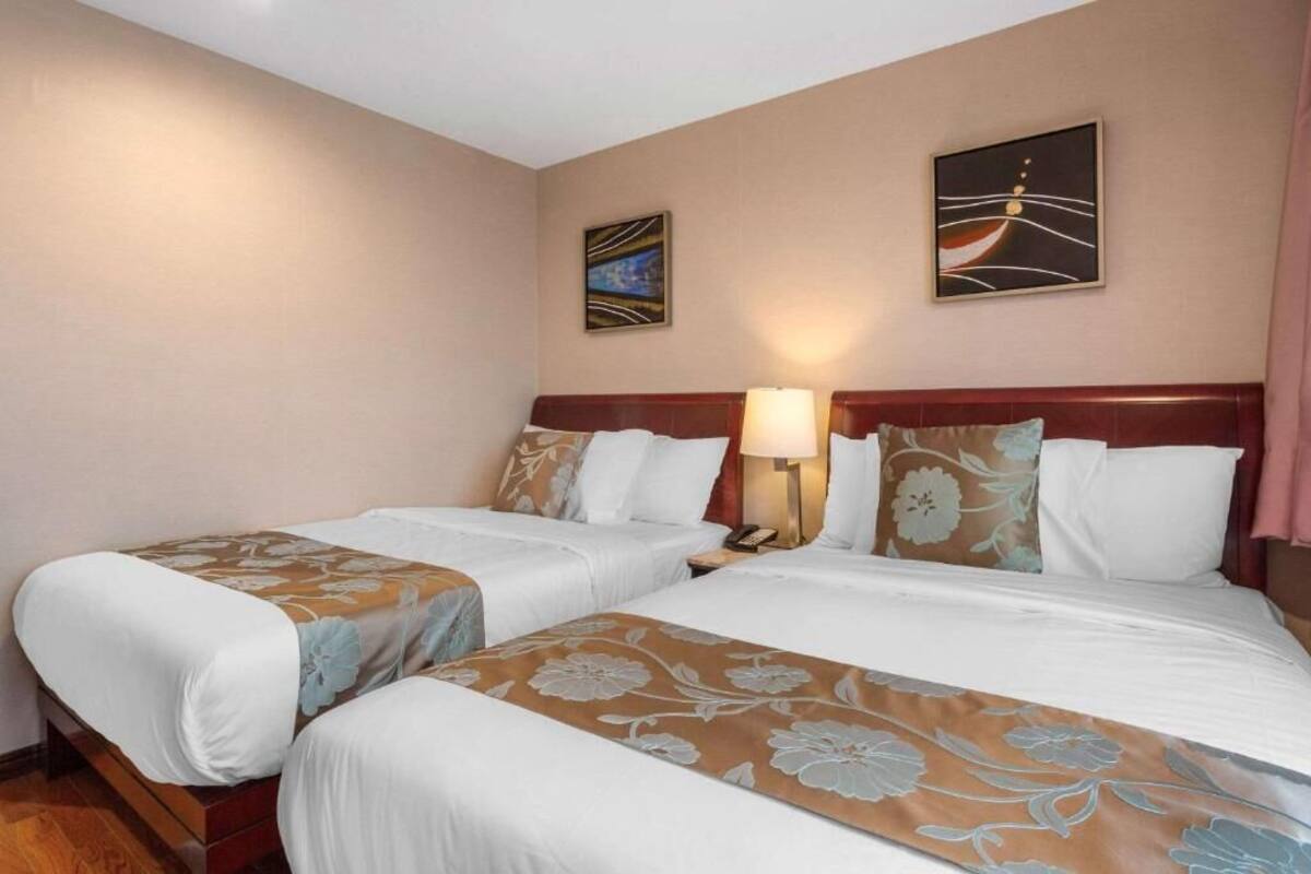 A hotel room with two beds, each with a floral bedspread, a wooden headboard, and a nightstand with a lamp.