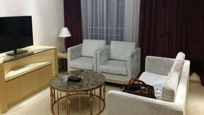 Een moderne woonkamer met een flatscreen televisie, een ronde salontafel, twee fauteuils, een bank en een lamp.