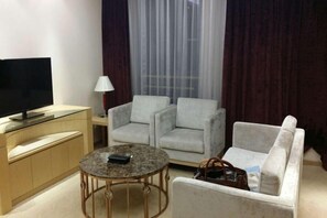 Una sala moderna con un televisor de pantalla plana, una mesa de centro redonda, dos sillones, un sofá y una lámpara.