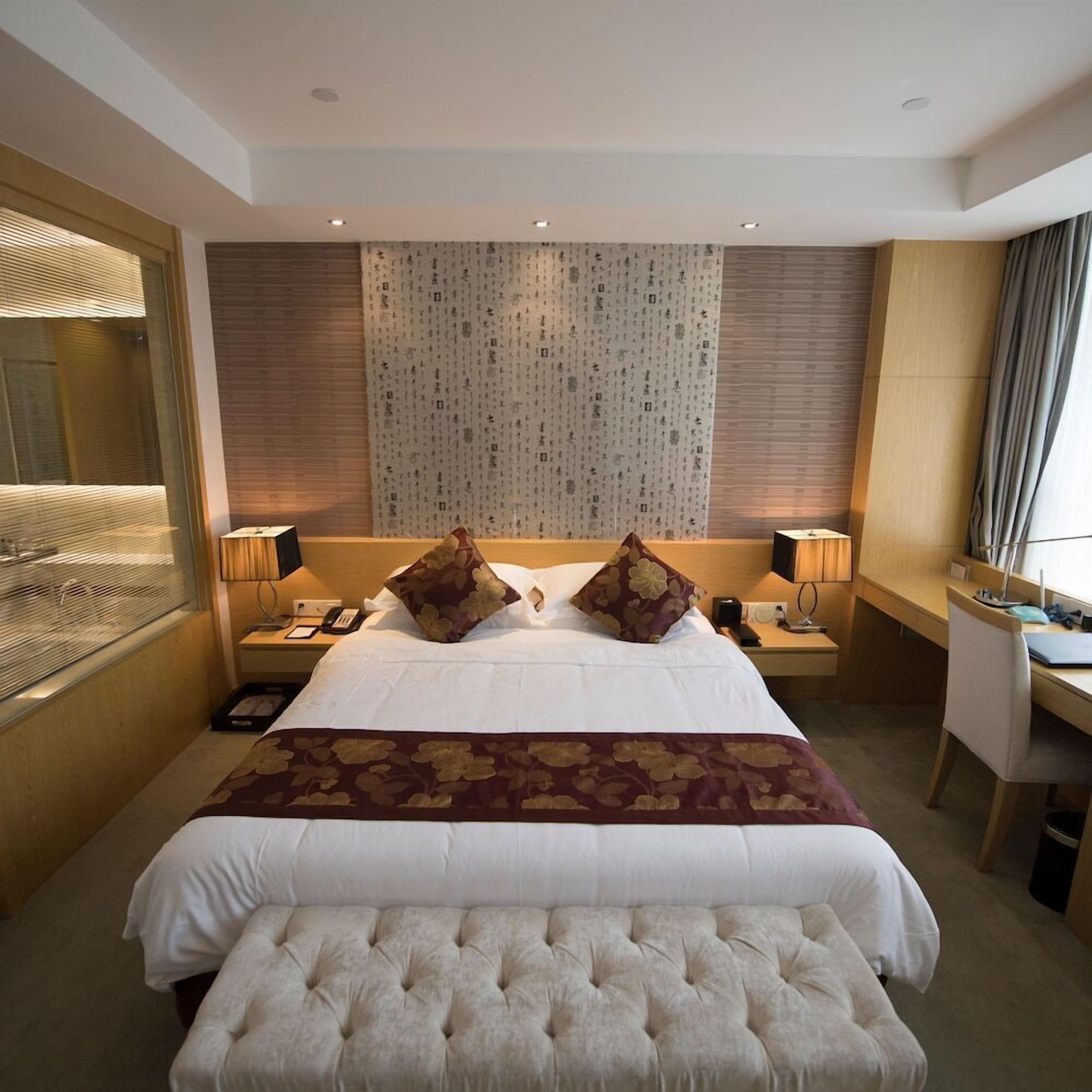 Quarto de hotel com uma cama grande, duas mesas de cabeceira, uma escrivaninha e uma cadeira.
