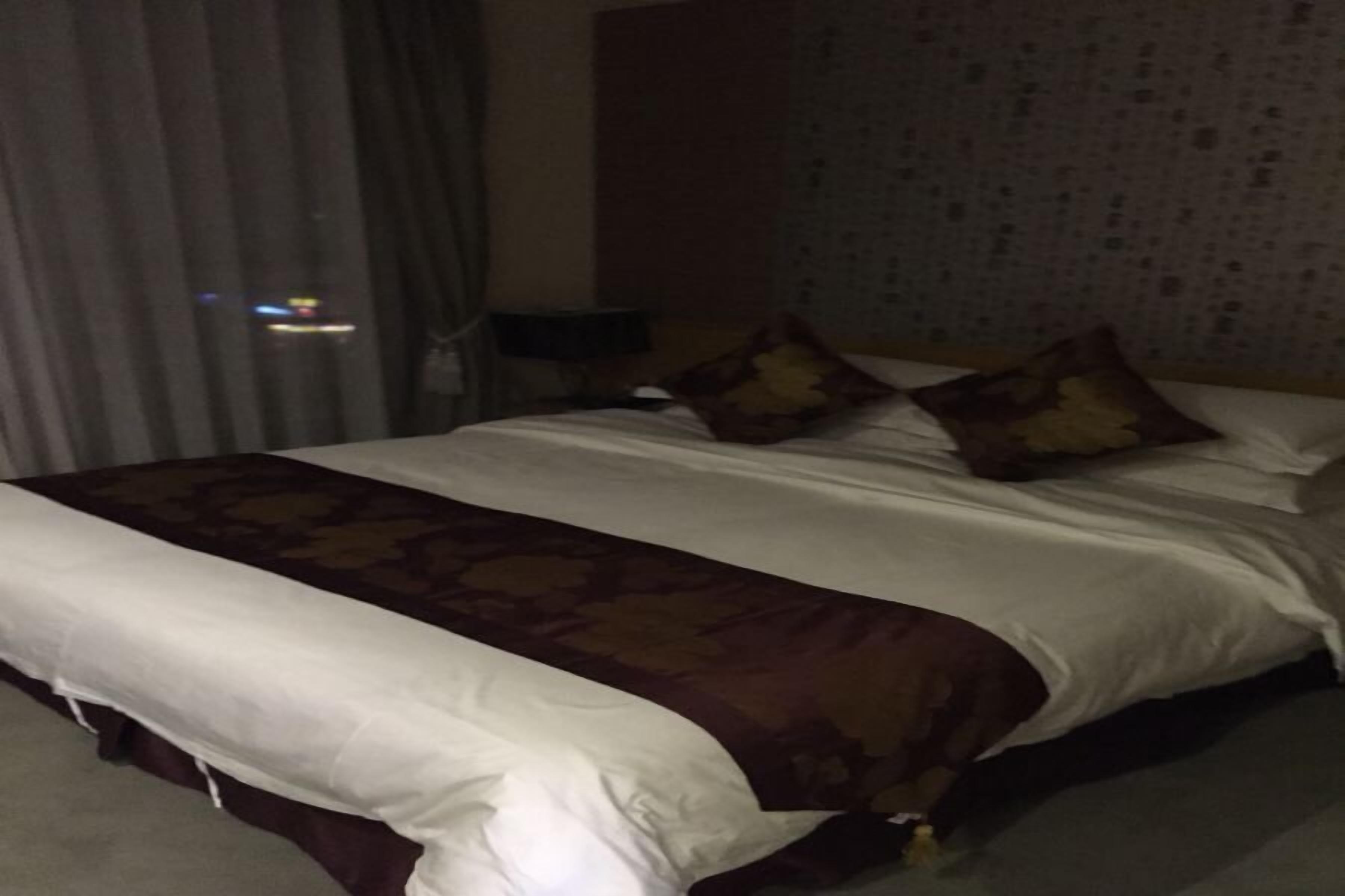 Habitación de hotel con una cama grande, una colcha estampada y un cabecero frente a una pared con textura.