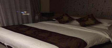 Habitación de hotel con una cama grande, una colcha estampada y un cabecero frente a una pared con textura.