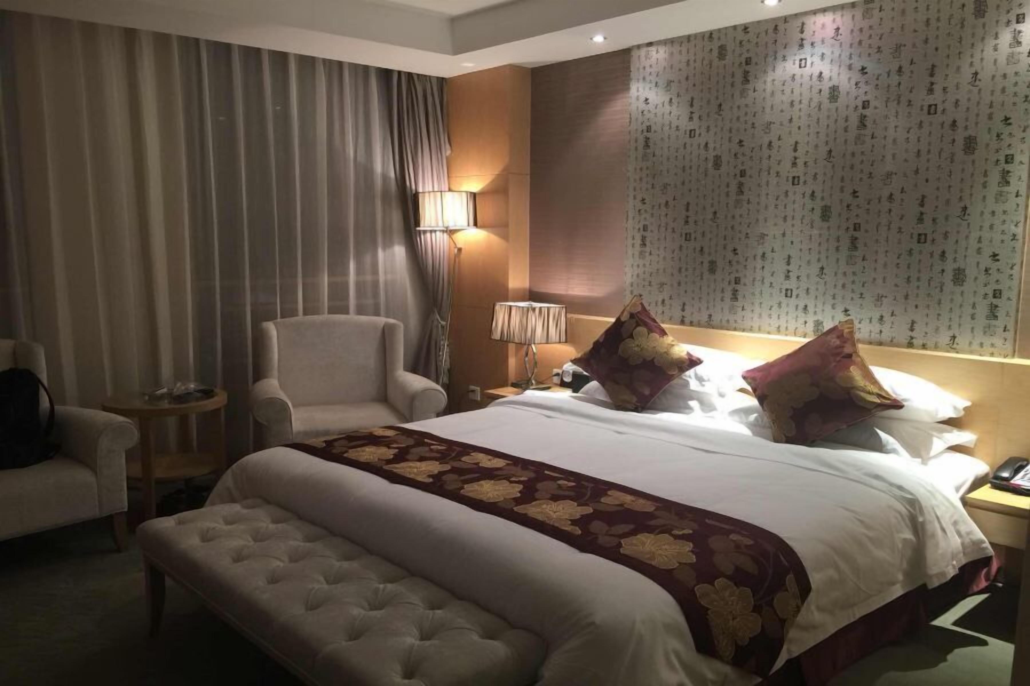 A hotel room with a large bed, a chair, a bedside table, and a lamp.