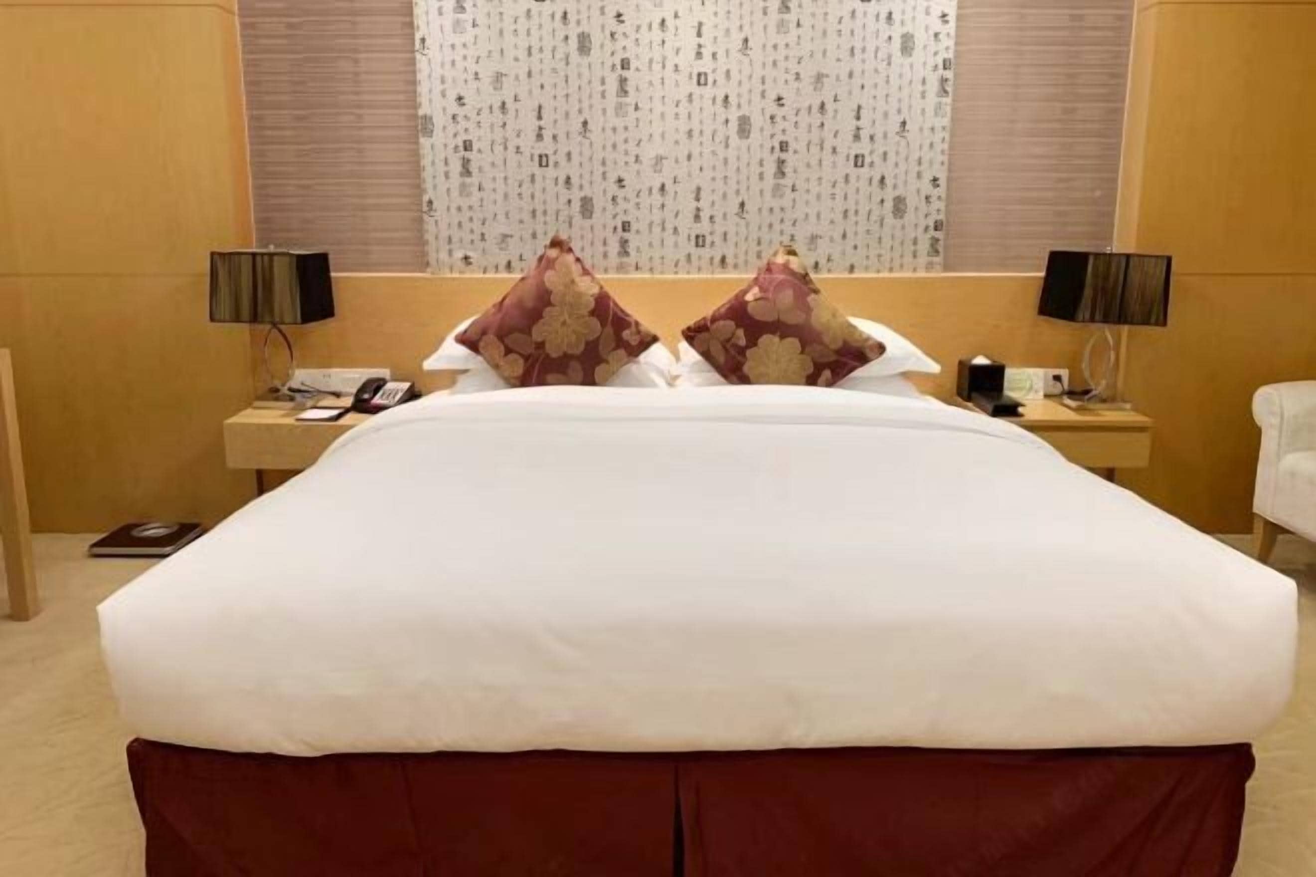 A hotel room with a large bed, two nightstands, a telephone, and a window with patterned curtains.
