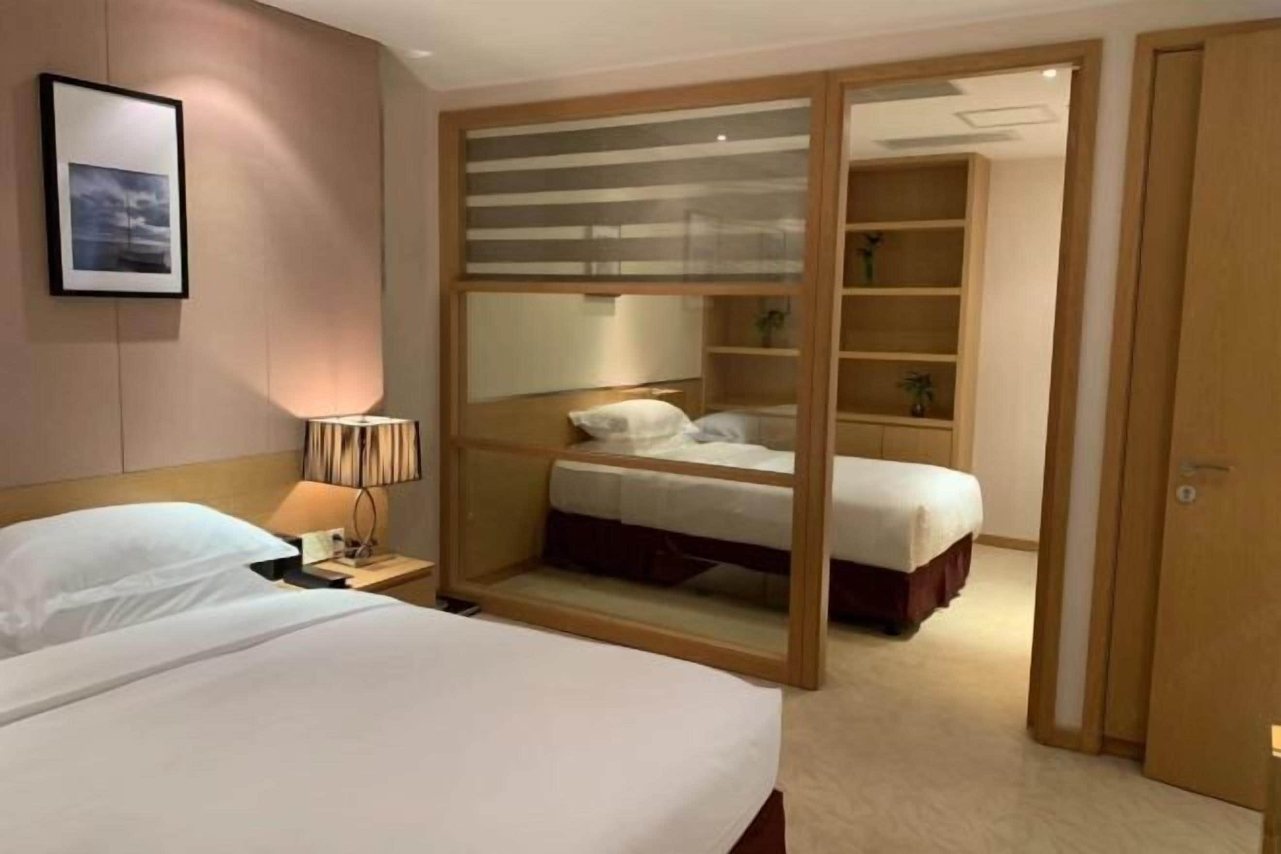 A hotel room with two beds, a nightstand with a lamp, a large mirror, and a wooden wardrobe.