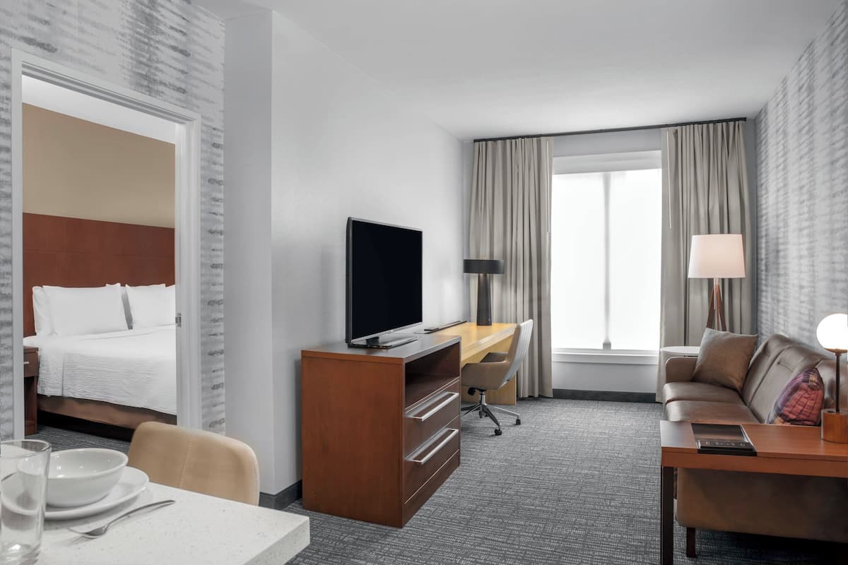 A hotel room with a bed, a desk with a TV, a sofa, and a dining table.