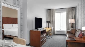 Una habitación de hotel con cama, escritorio con televisor, sofá y mesa de comedor.