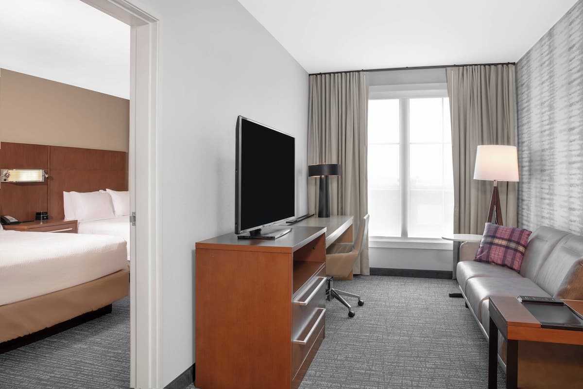 A hotel room with a bed, a desk with a TV, a sofa, and a window with curtains.