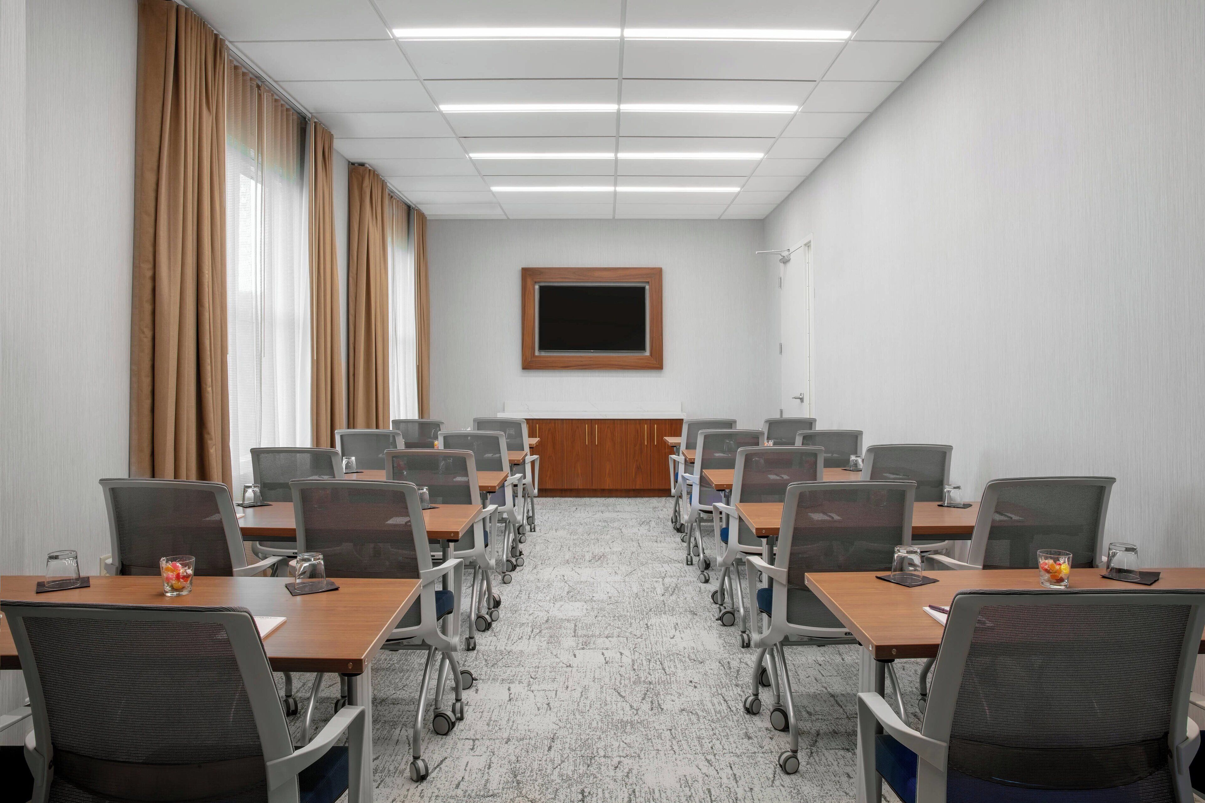 Un salón de conferencias con una larga mesa, sillas, una pantalla y un panel de madera en la pared.