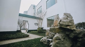 A modern building with a white exterior, a stone pathway, and a small garden area. - Songling Hotel (Suzhou)
