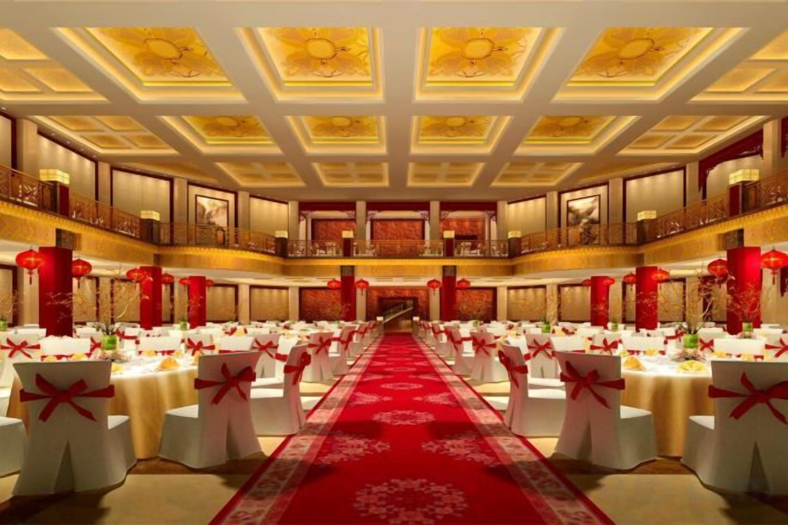 A banquet hall with a central aisle, tables with white tablecloths, and red decorations.