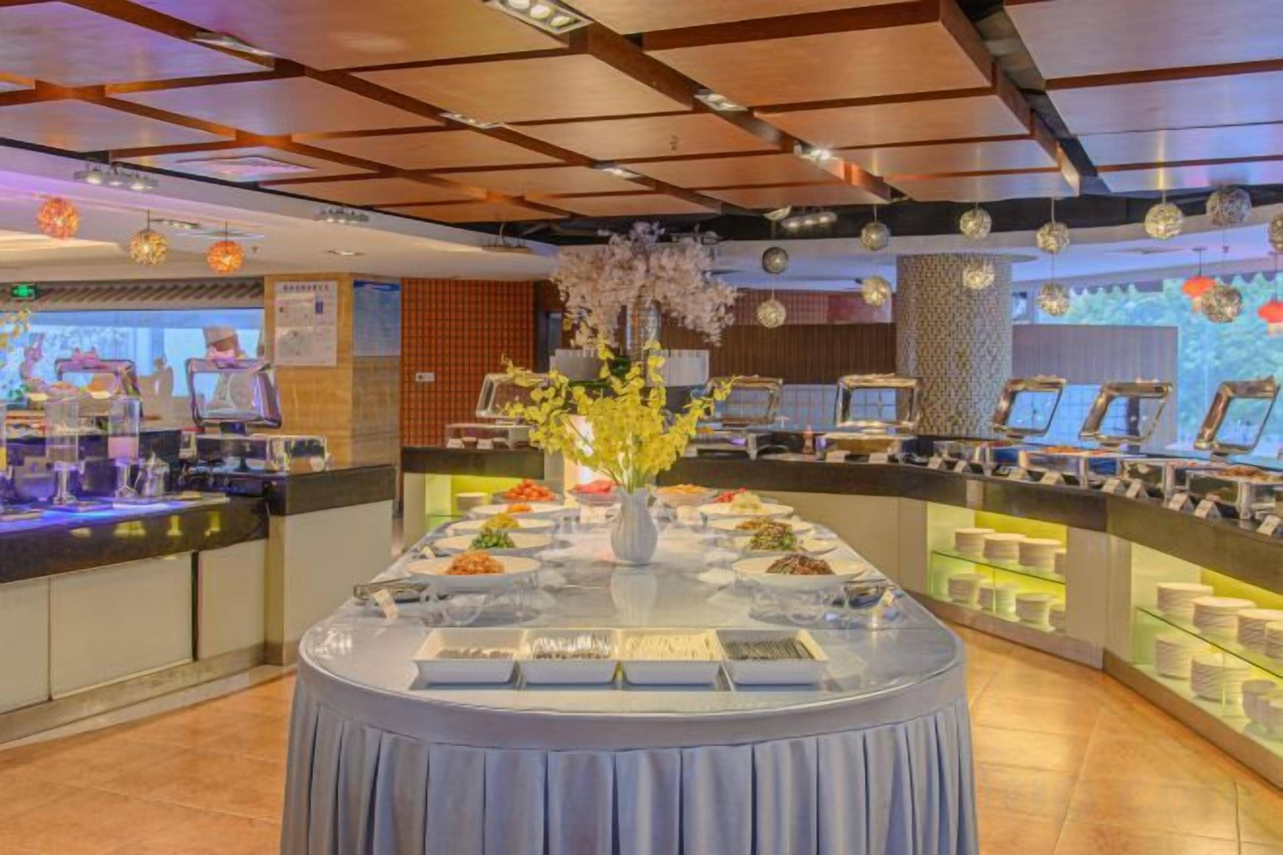 A buffet setup with a central round table, multiple food display cases, and a decorative vase with flowers.