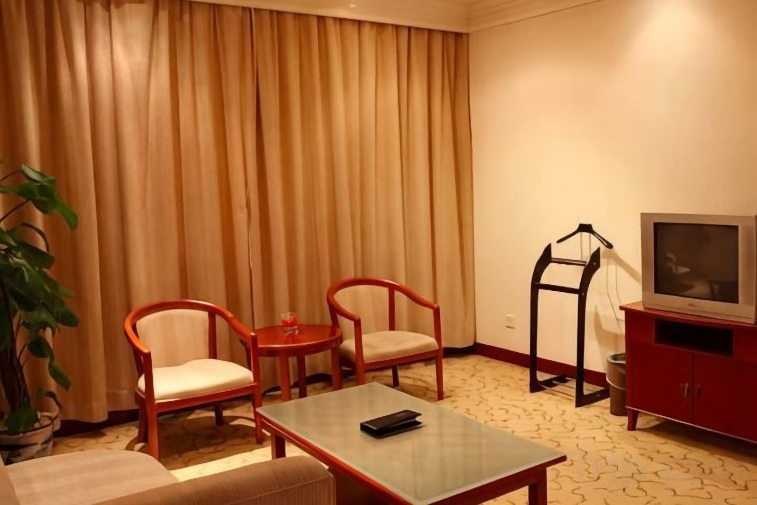 A hotel room with a sofa, two armchairs, a small table, a TV, and a plant.