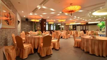 A banquet hall with round tables, chairs, and overhead lighting fixtures.